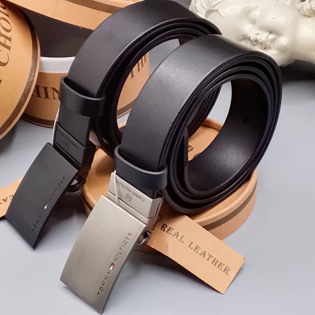 Black leather belt with silver buckle on a gray surface, surrounded by branded leather products.