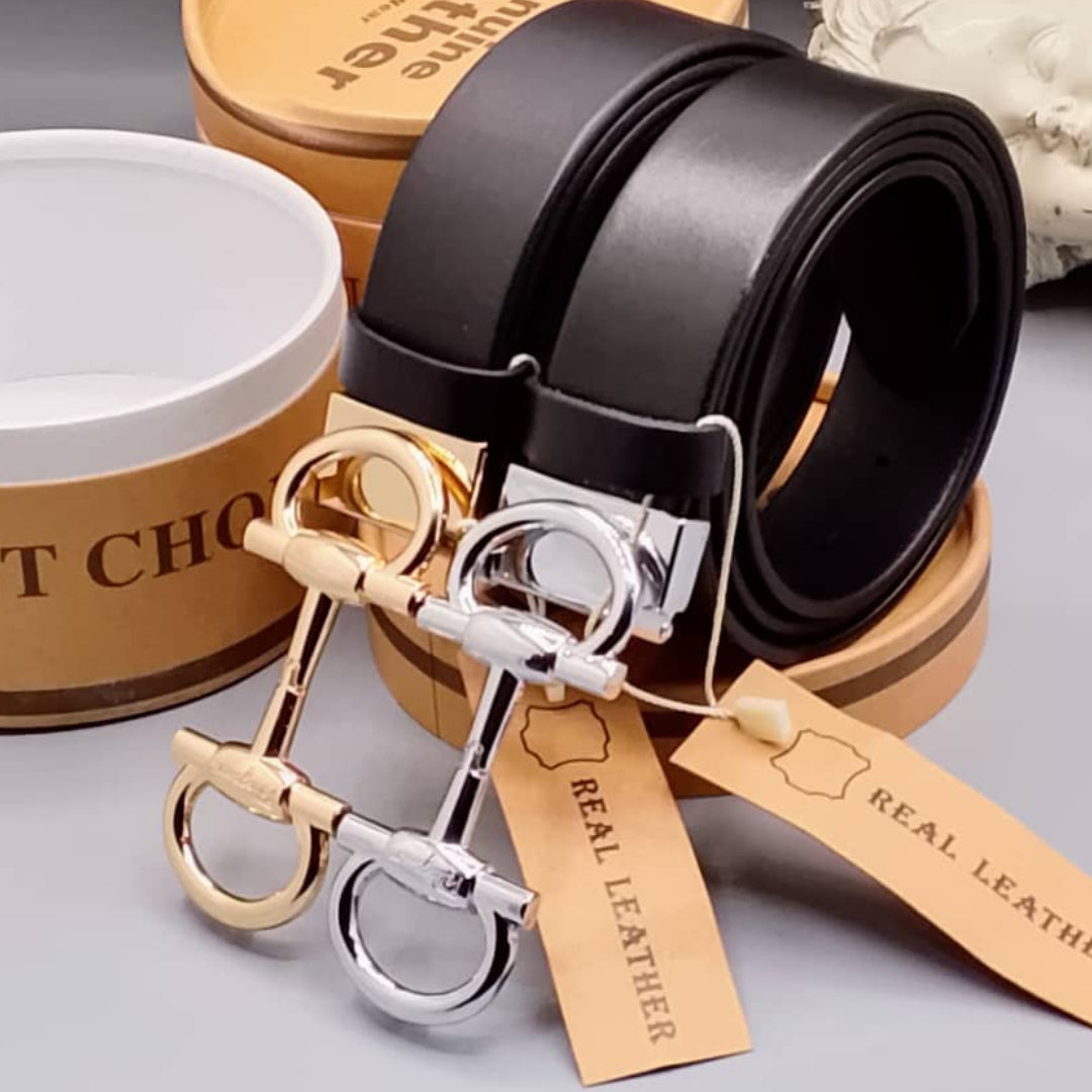 Black leather belt with gold and silver horse bit keychains on a gray surface.